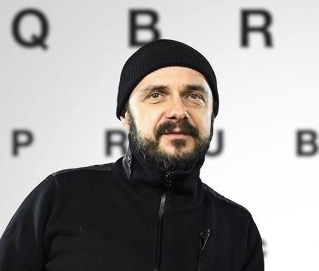 Arkadiusz Jakubik, wokalista zespołu Dr Misio, podczas energicznego występu na scenie, śpiewający do mikrofonu, z rozmazanym tłem świateł i muzyków, oddający atmosferę koncertu rockowego.