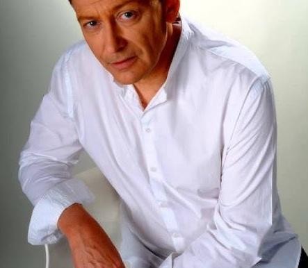 Jacek Borkowski na scenie, uśmiechnięty, w dynamicznej pozie, z mikrofonem lub w teatralnym oświetleniu, symbolizujący jego wszechstronną karierę aktorską i wokalną.