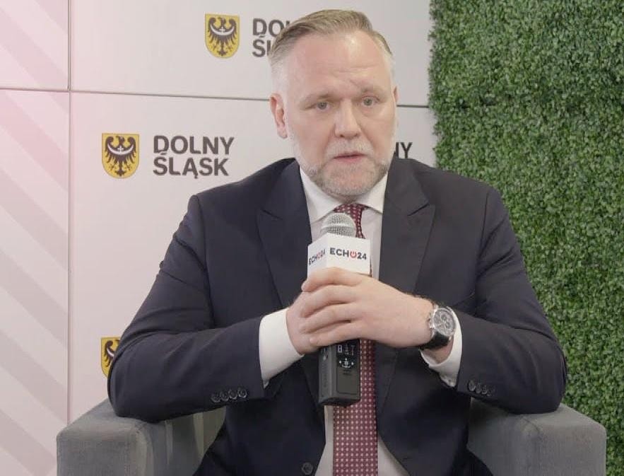Dawid Jackiewicz przemawiający na wiecu politycznym, z gestykulacją, w tle zamazany tłum.
