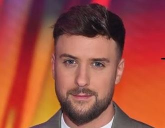 Aleksander Tomasz Sikora w spontanicznym ujęciu, śmiejący się lub rozmawiający, w tle studio telewizyjne lub wydarzenie medialne.