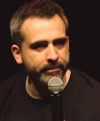 Abelard Giza podczas występu stand-upowego na scenie, w trakcie żartowania, z ekspresyjną mimiką.