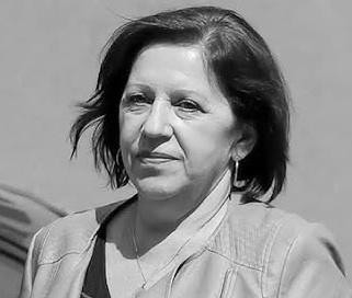 Barbara Skrzypek podczas przesłuchania w prokuraturze, siedząca przy stole w formalnym biurze, z poważnym, lecz opanowanym wyrazem twarzy.