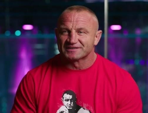 Mariusz Pudzianowski w oktagonie MMA, w trakcie walki, prezentujący swoją siłę i skupienie.
