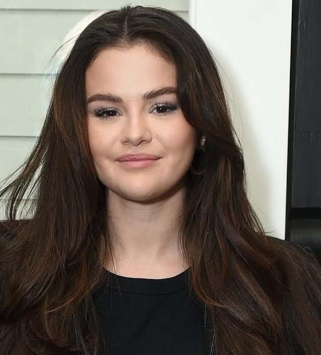 Selena Gomez występuje na scenie, śpiewając do mikrofonu, otoczona dynamicznym oświetleniem koncertowym.