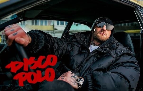 Kizo podczas energicznego występu na scenie, z mikrofonem w ręku i światłami scenicznymi w tle.